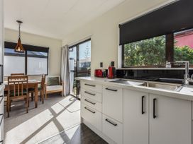 A kitchen with white cabinets and a countertop next to a dining area with a wooden table and chairs at Tahunanui Shoreside - Nelson Holiday Home in Tahunanui Beach