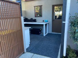 An outdoor area with a brown wooden fence a gray carpeted floor a white table with items on it a brown door and a small window at Tahunanui Shoreside - Nelson Holiday Home at Tahunanui Beach