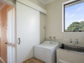 A laundry room with a washing machine a stainless steel sink window and a sliding door at Coastal Drift - Waikanae Beach Holiday Home in Waikanae Beach