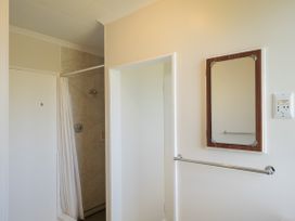 A bathroom with a shower area with a white curtain a wall mirror a towel bar and a shavers only power outlet at Coastal Drift - Waikanae Beach Holiday Home Waikanae Beach