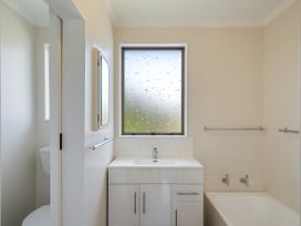A bathroom with a sink cabinet a bathtub and a frosted window at Coastal Drift - Waikanae Beach Holiday Home in Waikanae Beach