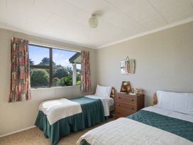 A bedroom with two single beds a wooden dresser and a window with curtains at Coastal Drift - Waikanae Beach Holiday Home in Waikanae Beach