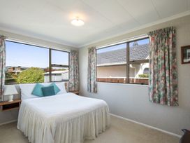A bedroom with a bed with white bedding and three pillows next to two windows with floral curtains at Coastal Drift - Waikanae Beach Holiday Home Waikanae Beach
