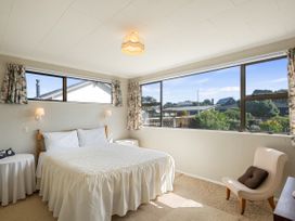 A bedroom with a bed side tables and an armchair next to large windows at Coastal Drift - Waikanae Beach Holiday Home in Waikanae Beach