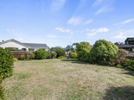 A backyard with grass and bushes surrounded by wooden fences and houses in the background at Coastal Drift - Waikanae Beach Holiday Home in Waikanae Beach