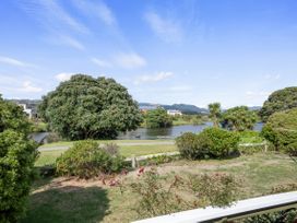 A backyard with grass and bushes overlooking a lake with trees and houses in the distance at Coastal Drift Waikanae Beach