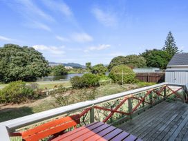 A wooden deck with a table and railing overlooking a garden with bushes and a lake in the background at Coastal Drift Waikanae Beach