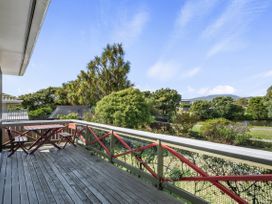 A wooden deck with a table and chairs overlooking trees and a river at Coastal Drift - Waikanae Beach