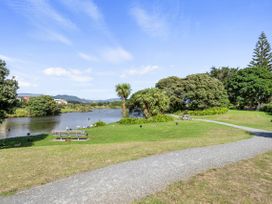 A park with a pond trees picnic tables and a gravel path at Coastal Drift - Waikanae Beach Holiday Home in Waikanae Beach