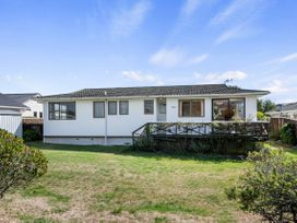 A backyard with grass and bushes and a white single-story house with a porch and windows at Coastal Drift - Waikanae Beach Holiday Home in Waikanae Beach