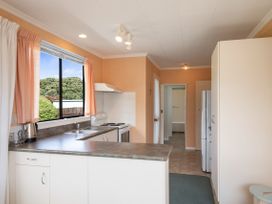 A kitchen with countertops a stove a sink a refrigerator and a window with curtains at Coastal Drift - Waikanae Beach Holiday Home in Waikanae Beach