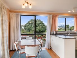 A dining area with table and chairs next to large windows and a kitchen counter at Coastal Drift - Waikanae Beach Holiday Home in Waikanae Beach