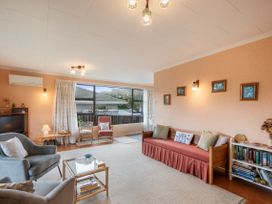 A living room with armchairs a sofa a coffee table a television and large windows at Coastal Drift Waikanae Beach Holiday Home in Waikanae Beach