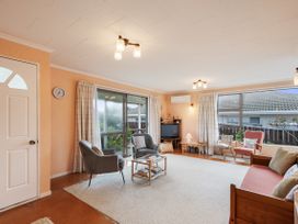 A living room with chairs a sofa a coffee table and a television at Coastal Drift - Waikanae Beach Holiday Home in Waikanae Beach