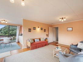 A living room with a sofa, armchairs, a small coffee table, and a dining area with a table and chairs near a window at Coastal Drift - Waikanae Beach Holiday Home in Waikanae Beach