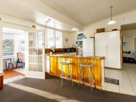 A kitchen with a wooden counter and two metal stools next to a white refrigerator and cabinets at Haere Mai Reefton Heritage Holiday Home in Reefton