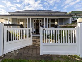 A white gate open to a pathway leading to a gray house with columns and a porch at Haere Mai Reefton Heritage Holiday Home in Reefton