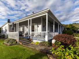 A wraparound porch with outdoor furniture and an umbrella on a grassy yard at Haere Mai Reefton Heritage Holiday Home in Reefton