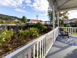 A porch with a single chair and patterned rug overlooking a garden with flowers and bushes at Haere Mai Reefton Heritage Holiday Home in Reefton