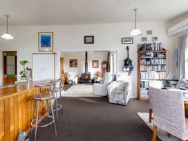 A living area with a wooden bar counter with stools a bookshelf a guitar on the wall and a wood stove in an adjacent room at Haere Mai Reefton Heritage Holiday Home in Reefton
