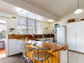 A kitchen with wooden countertops two metal bar stools a white refrigerator and white cabinets at Haere Mai Reefton Heritage Holiday Home in Reefton