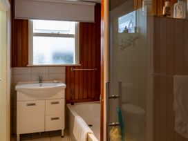 A bathroom with a sink and cabinet next to a bathtub with a towel hanging on the side and a toilet behind a glass door at Haere Mai Reefton Heritage Holiday Home in Reefton