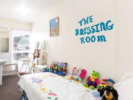 A small room with a bed and stuffed animals a bookshelf a high chair and a mirror on the wall at Haere Mai Reefton Heritage Holiday Home in Reefton