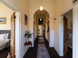 A hallway with rugs on the floor and a small table with flowers on the left wall and open wooden doors leading to bedrooms at Haere Mai Reefton Heritage Holiday Home in Reefton