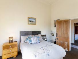 A bedroom with a bed a wooden bedside table a chair a bookshelf and an open wooden door at Haere Mai Reefton Heritage Holiday Home in Reefton