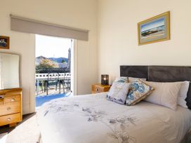 A bedroom with a bed with pillows next to wooden nightstands and a door leading to a balcony at Haere Mai Reefton Heritage Holiday Home in Reefton