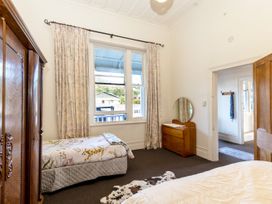 A bedroom with two beds a wooden wardrobe a dresser with a round mirror and floral curtains at Haere Mai Reefton Heritage Holiday Home in Reefton