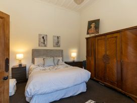 A bedroom with a bed and pillows two bedside tables with lamps a large wooden wardrobe and paintings on the wall at Haere Mai Reefton Heritage Holiday Home in Reefton