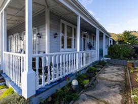 A house porch with white railings blue walls outdoor chairs and a garden path at Haere Mai Reefton Heritage Holiday Home in Reefton