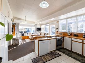 A kitchen with white cabinets and wooden countertops next to a dining area with a round table and chairs at Haere Mai Reefton Heritage Holiday Home in Reefton