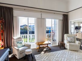 A living room with two armchairs a small wooden table and glass sliding doors leading to a balcony at Haere Mai Reefton Heritage Holiday Home in Reefton