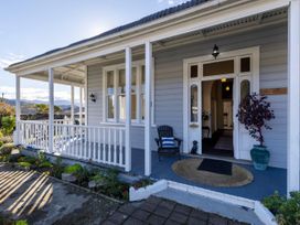 A front porch with white railings a chair with a cushion and a potted plant at Haere Mai Reefton Heritage Holiday Home in Reefton