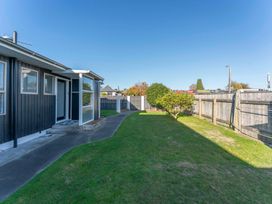 A backyard with lawn and small trees beside a house with a concrete pathway at King's Crossing - Your Taupo Getaway in Taupo Central