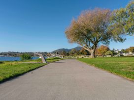 A paved walkway with grass on both sides and a large tree by the side near a body of water at King's Crossing - Your Taupo Getaway in Taupo Central