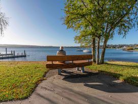 A person sitting on a wooden bench by a lakeside with boats on the water and trees nearby at King's Crossing - Your Taupo Getaway in Taupo Central