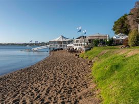 A sandy beach with a sailing club building and flags near calm water at King's Crossing - Your Taupo Getaway in Taupo Central