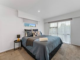 A bedroom with a bed with blue bedding and multiple pillows a black side table with a lamp and large window with sheer curtains at King's Crossing - Your Taupo Getaway! in Taupo Central