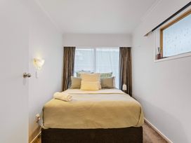 A bedroom with a bed, pillows, a towel, small window with decoration, wall light, and curtains at King's Crossing - Your Taupo Getaway in Taupo Central