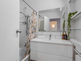 A bathroom with a bathtub and shower curtain a white vanity with a faucet a large mirror and bottles on the counter at King's Crossing - Your Taupo Getaway in Taupo Central