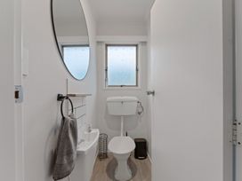 A small bathroom with a toilet a small sink a round mirror a towel on a ring and a window at King's Crossing - Your Taupo Getaway Taupo Central