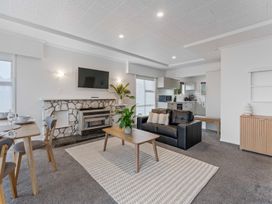 A living room with a black leather sofa wooden coffee table and stone fireplace next to a dining area and kitchen at King's Crossing - Your Taupo Getaway in Taupo Central