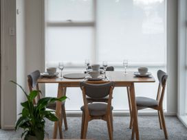 A dining table set with bowls, plates, wine glasses, and cutlery with four chairs and a plant in a modern room at King's Crossing - Your Taupo Getaway in Taupo Central