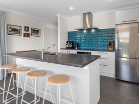 A kitchen with a black countertop island and four wooden stools at Bennett's Bach - Waipu Holiday Home in Waipu