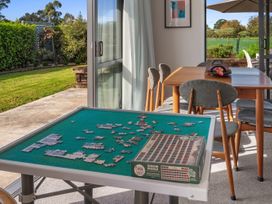 A puzzle table with pieces and box next to a wooden dining table with chairs by a patio door at Bennett's Bach - Waipu Holiday Home in Waipu
