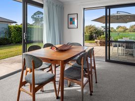 A dining area with a wooden table and six chairs next to large glass sliding doors leading to an outdoor patio at Bennett's Bach - Waipu Holiday Home in Waipu