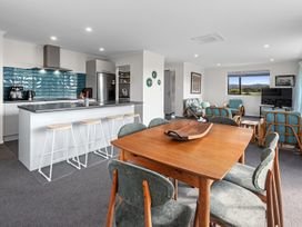 An open plan kitchen and living area with a wooden dining table and green chairs and bar stools at Bennett's Bach - Waipu Holiday Home in Waipu
